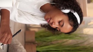 Dikey video. Günlük boş zaman. Hobi yazıyorum. Hafta sonu evde. Hayal ürünü, kulaklıklı, rahat bir odada, günlükte yazan bir kadın..