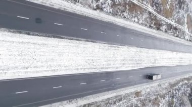 Dikey video. Drone kış manzarası. Karlı yol kaldırımı. Beyaz donmuş yol trafiği orman bulutlu bir günde araba yolunu geçiyor..