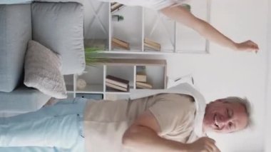 Dikey video. Aile eğlencesi. Komik dans. Dost canlısı anne-baba ve kız atlıyor. Birlikte hareket ediyorlar. Aydınlık ev içinde heyecanlı hissediyorum..