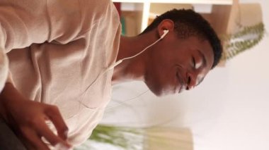 Dikey video. Ev meditasyonu. Yoga sakinliği. Ses rahatla. Rahatlık ve rahatlık. Huzurlu sakin adam oturma odasındaki koltukta kulaklıkla müzik dinliyor..