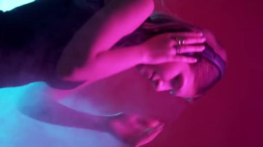 Dikey video. Neon ışığı müziği. 90 'ların partisi. Çok neşeli bir kadın, kulaklıkla en sevdiği şarkıyı dinliyor. Geceleri dans ediyor. Renkli, canlı bir duman..