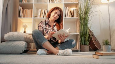 İlginç bir kitap. İlham verici bir kadın. Ev tatili. Orta yaşlı bir kadın yerde oturuyor ve aydınlık odada kitap okumaktan zevk alıyor..