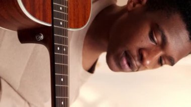 Dikey video. Gitar dersi. Müzik dersi. İnternetten enstrüman dersi. Neşeli öğrenci sanatçı evde internet kursunda şarkı akorları öğreniyor..