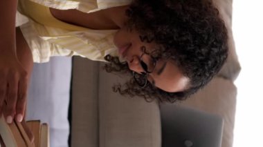 Dikey video. Kitap eğleniyor. Bilgi ve rahatlık. Evde dinleniyorum. Huzurlu kadın öğrenci kitap okuyor rahat bir odada halının üzerinde dinleniyor..