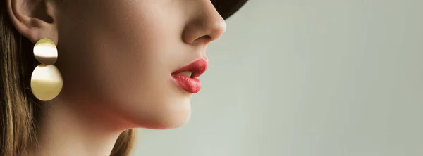 Lips makeup. Cosmetic trend. Unrecognizable young beautiful woman in juicy red lipstick perfect face skin golden earring on grey background empty space.