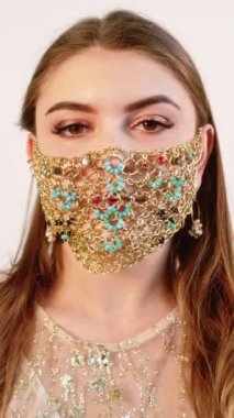 Dikey video. Pandemik moda. DIY aksesuarı. Esrarengiz esmer kadın altın zincirli yüz maskesi ile poz veriyor..