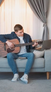 Gitar kursu. İnternet müzik dersi. Yaratıcı hobi. Evdeki kanepede dizüstü bilgisayarda telli çalgılar çalmayı öğrenen ilham verici bir adam..