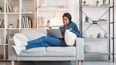 İnternetten tartışıyorlar. Video toplantısı. Hayal kırıklığına uğramış bir kadın dizüstü bilgisayarda ilişki sorunu hakkında tartışıyor evdeki oturma odasında kanepede sohbet ediyor..