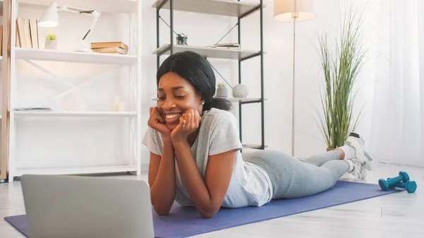 Online fitness. Video communication. Young sporty woman talking at laptop internet virtual chat meeting on yoga mat after exercising in home living room.
