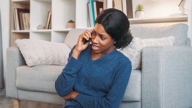 Telefon konuşması. Hücresel iletişim. Ev içi rahatlık. Keyifli, rahat bir kadın mobil cihazla konuşuyor. Oturma odasındaki rahat koltukta dinleniyor..