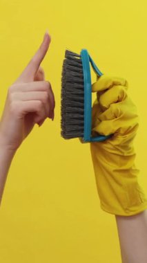 Dikey video. Sert fırça. Temizlik reklamı. Sarı arka planda izole edilmiş iyi kalitede çamaşır fırçası dokunuşunu gösteren koruyucu eldivenler veren kadın..