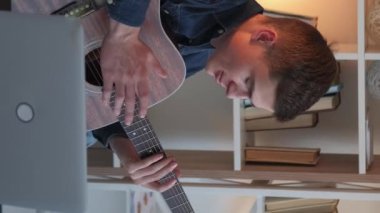 Dikey video. Çevrimiçi müzik dersi. Gitar dersi. Uzaktan eğitim. Evdeki dizüstü bilgisayar konferansında telli çalgılar dersi veren adam..