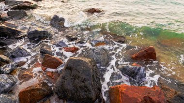 Deniz dalgası. Deniz kenarı geçmişi. Deniz doğası güzelliği. Beyaz köpüklü berrak su kahverengi gri kayaların üzerinde süzülüyor güzel sahil şeridi.
