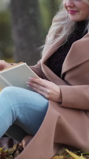 垂直录像 有趣的书快乐的女人秋天放松 微笑的女士坐在地上用树叶看书 — 图库视频影像