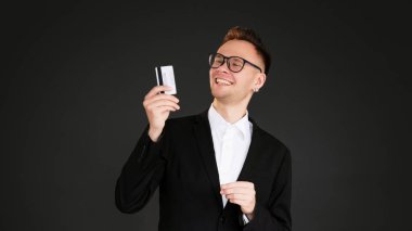 Banka servisi. Nakitsiz ödeme. Samimi gülümseyen iş adamı müşterisi kredi kartını koyu siyah boş bir arkaplanda izole etmiş..