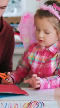 Dikey video. Yaratıcı ders. Anaokulu sanatı. Yetenekli çocukların stüdyosundaki küçük kız öğrencilere renkli kağıt origami dersi veriyor..