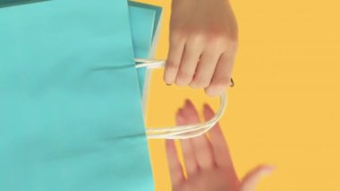 Dikey video. Alışveriş teslimatı. Perakende satış. Kadın müşteri eli Kara Cuma sezonu indirimini alıyor. Kağıt çantalar. Turuncu arka planda ayrılan hediye..