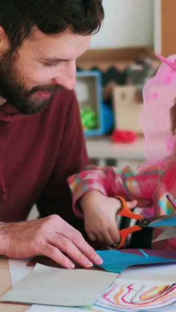 垂直录像 手工制作的儿童礼物 父亲的帮助快乐的父亲支持着充满热情的女儿 小女孩的业余爱好就是在桌旁剪彩纸 — 图库视频影像