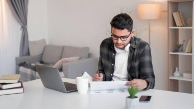 Veri analizi. İş raporu. Odaklanmış hesap yöneticisi profesyonel pazarlama grafikleri üzerinde çalışıyor. Ev dizüstü bilgisayarında notlar yazıyor..