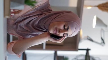 Dikey video. Cep telefonu konuşması. İş görüşmesi. Mutlu kadın yönetici telefonda konuşuyor. Ev ofis masaüstünde mobil şirket iletişiminin keyfini çıkarıyor..