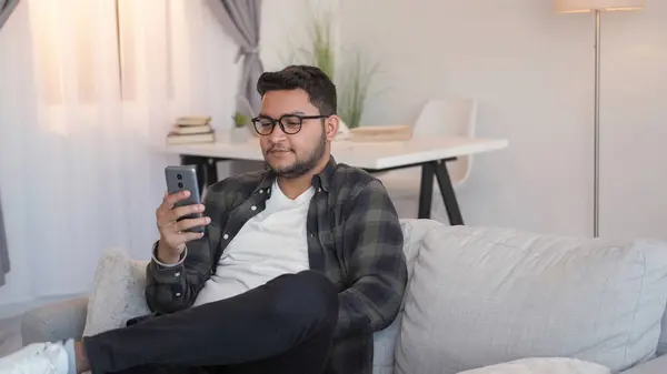Video phone call. Virtual communication. Device leisure. Cheerful man talking on cell social media online chat on cozy sofa in home living room.
