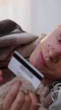 Dikey video. Çevrimiçi ödeme. İlaç siparişi. Ekose kumaşla kaplı hasta bir adamı hapşırtmak akıllı telefondan evde yatan internet işlemleri için kredi kartı numarası yazmak..