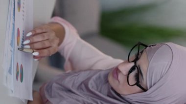 Dikey video. Analiz raporu. Gelir tabloları. Finansal strateji. Ciddi konsantre kadın muhasebeci ofis masasındaki iş istatistikleri araştırma grafiklerini kontrol ediyor..