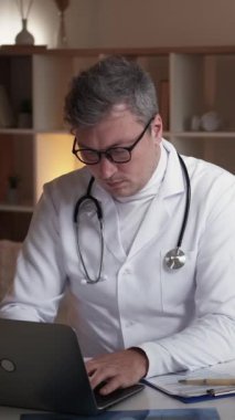 Dikey video. Sağlık raporu. Dijital sağlık hizmeti. Bilgisayarda daktilo yazan yoğun doktor modern hastanenin iş yerinde masa başında oturuyor..