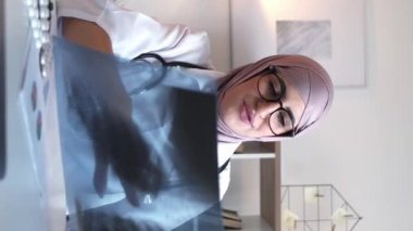 Dikey video. İnternet tıbbı. Uzaktan kumandalı. TeleHealth teşhisi. Kadın doktor klinikteki internet aramasında zatürree tedavisi için akciğer röntgeni danışmanlığını inceliyor..