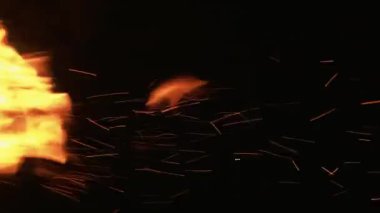 Dikey video. Alev kıvılcımlar saçar. Siyaha ateş. Sarı turuncu renkte, parlak şenlik ateşi, karanlık, boş ve soyut arka planda alevleniyor..