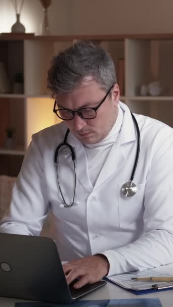 垂直录像 医疗报告 数字医疗 专心致志的医生男人坐在现代医院工作场所的办公桌前 用笔记本电脑打字 — 图库视频影像