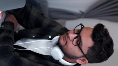 Dikey video. İnternet keyfi. Dizüstü bilgisayar eğlencesi. Sakin genç adam internette bilgisayar sörfü yapıyor evdeki sosyal medya dijital içeriğini inceliyor.