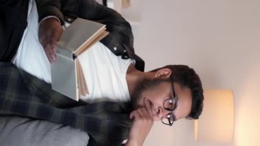 Dikey video. Boş zamanlarımda kitap okurum. Hafta sonu evde. Odaklanmış, gözlüklü zeki genç adam oturma odasındaki kanepede dinlenerek en çok satan hikayeleri okuyordu..