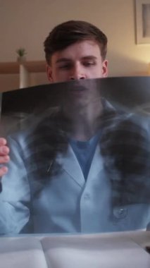 Dikey video. Radyoloji doktoru. Tıbbi teşhis. Profesyonel sağlık hizmeti. Online randevu. Akciğer röntgeni olan bir doktor hastane çalışma alanındaki sanal toplantıda danışmanlık yapıyor..