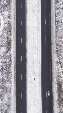Dikey video. Hava karlı yolu. Kış manzarası. Beyaz donmuş orman ağacı asfalt şeritli, geçen arabalar bulutlu kırsal yol kaldırımlı..