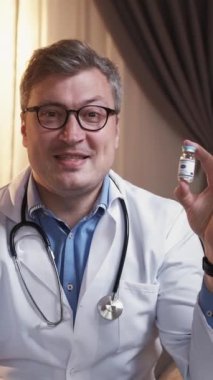 Dikey video. Hastalık tedavisi. Doktor internet araması. Çevrimiçi tıp konferansı. İki aşı şişesi olan zeki bir adam aydınlık odadaki sanal buluşmada danışmanlık yapıyor..