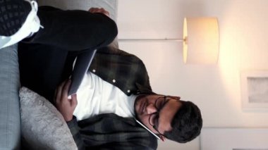 Dikey video. İş görüşmesi. Başlangıç tartışması. Mobil iletişim. Ciddi meşgul bir çalışan telefonda konuşuyor. Ofisteki kanepede istatistik analizi yapıyor..