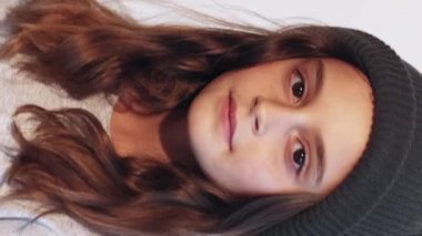 Dikey video. Güzel çocuk. Moda çocuğu. Sevimli hippi kız modeli siyah örgü şapka takıyor beyaz arka planda saçlara dokunuyor..