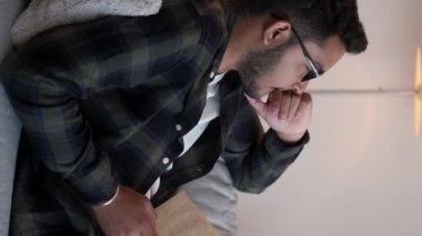 Dikey video. Yurt içi okumalar. Kitap haftasonu. Bilgi yaşam tarzı. Düşünceli genç bir erkek öğrenci. Oturma odasında dinlenirken kanepenin keyfini çıkarıyor..