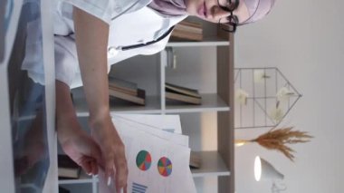 Dikey video. Tıbbi çizelgeler. Sağlık sigortası. Ciddi kadın doktor hastanedeki Webinar çağrı toplantısında istatistik grafiklerini tartışıyor..