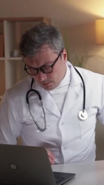 Dikey video. Radyoloji uzmanı. Sağlık çalışanı. Hastane bilgisayar raporu. Ciddi bir doktor. Akciğerleri röntgenli. Laptopta veri yazıyor..