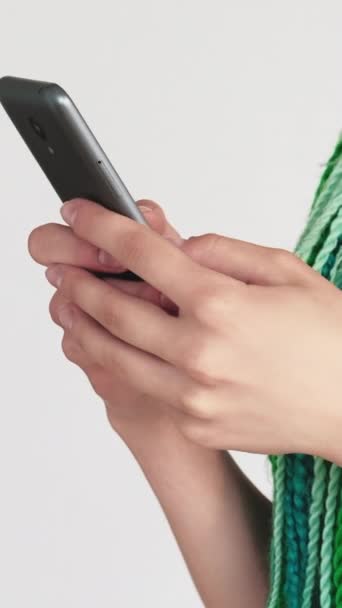 バーティカルビデオ モバイルチャット インターネットブラウジング 白い背景に隔離されたスマートフォンを使用してミントブルーヘアブレイドクリエイティブヘアスタイルの認識できない女性 — ストック動画