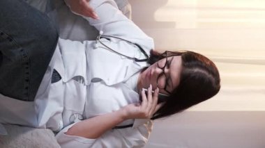 Dikey video. Yaralı teşhisi. Çalışan doktor. Sağlık sigortası. Ciddi bir kadın doktor, hastanede röntgen film danışmanlığı yapan bir hastayı muayene ediyor..