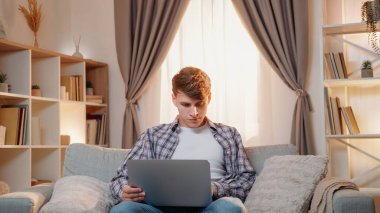 Online iş. Erkek işçi. Dijital teknoloji. Ciddi bir adam dizüstü bilgisayarını karıştırıyor. Açık evdeki koltukta oturuyor..