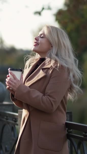 垂直录像 浪漫的心情 有灵感的女人秋天的美丽 快乐的女士呆在公园里喝着一杯咖啡感到快乐呼吸着空气慢动作 — 图库视频影像