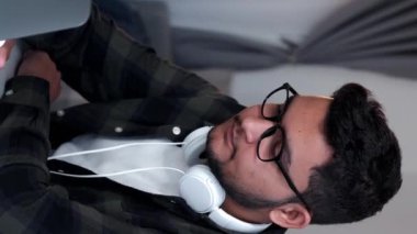 Dikey video. İnternet keyfi. Dizüstü bilgisayar eğlencesi. Sakin genç adam internette bilgisayar sörfü yapıyor evdeki sosyal medya dijital içeriğini inceliyor.