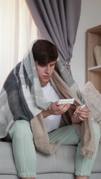 バーティカルビデオ ホームメディカル インフルエンザ治癒 居間の内部の冷たい処置のための薬を選ぶソファーに座って置かれた病気の男 — ストック動画