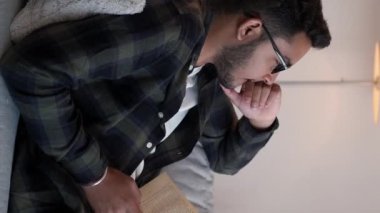 Dikey video. Yurt içi okumalar. Kitap haftasonu. Bilgi yaşam tarzı. Düşünceli genç bir erkek öğrenci. Oturma odasında dinlenirken kanepenin keyfini çıkarıyor..