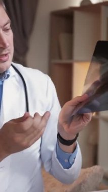 Dikey video. Teşhis konsültasyonu. Çevrimiçi doktor. Steteskoplu bir tıp uzmanı modern iç mekanda sanal atamada x-ray akciğer hastalığını açıklıyor..