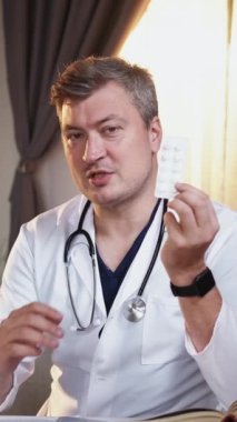 Dikey video. İlaç danışmanlığı. Erkek bir uzman. Çevrimiçi sağlık desteği. Tıbbi üniformalı doktor sanal konferansta ilaç etkisini açıklıyor..
